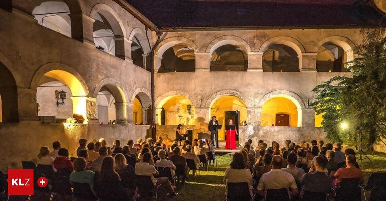 Eine nächtliche Aufführung unter einem alten Innenhof mit Bogenfenstern. Ein Mann und eine Frau singen auf der Bühne, während ein Publikum in Stühlen um sie herum sitzt.
