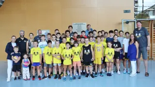Eine Gruppe junger Athleten in gelben und schwarzen Trikots steht in einer Sporthalle. Ein Mann steht in der Mitte, und eine Tafel mit Text ist an der Wand montiert.