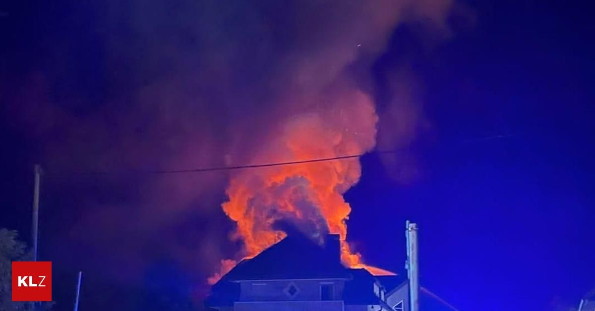Ein großes Feuer umhüllt ein Haus bei Nacht, mit intensiven Flammen und Rauch, der in den dunklen Himmel aufsteigt.