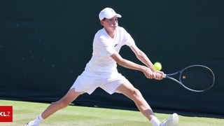 Ein Tennisspieler schwingt einen Schläger, um einen Ball auf einem Tennisplatz zu schlagen.