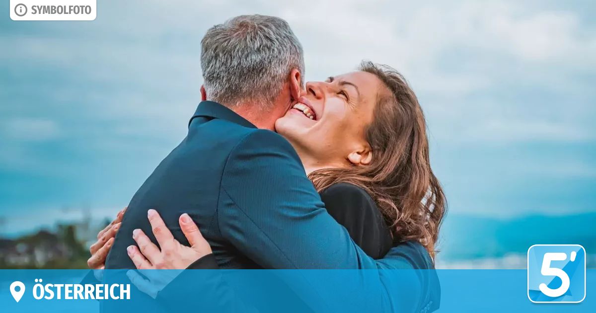 Ein Mann und eine Frau umarmen sich am Strand, lächeln und sehen glücklich aus.