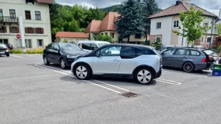 Ein hellblaues Auto steht in einem Parkplatz neben zwei anderen Autos. Die Gebäude hinter den Autos haben braune Dächer.