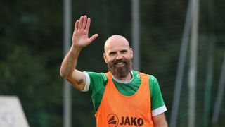 Ein Mann mit Bart winkt und trägt eine orange-grüne Jako-Weste.