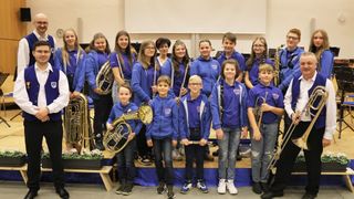 Eine Gruppe von Kindern und Jugendlichen in Blau posiert für ein Foto mit ihren Musikinstrumenten, darunter Trompeten, Flöten und Posaunen.