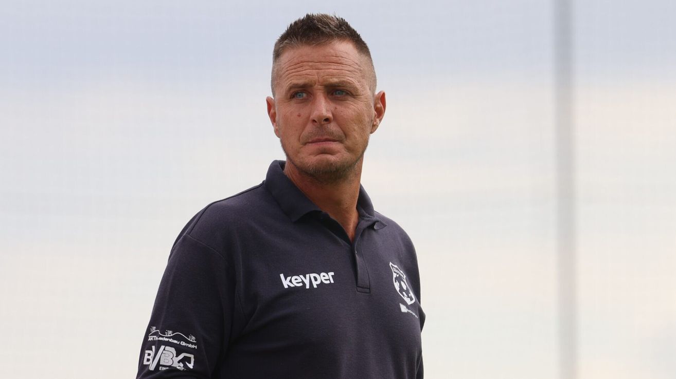 Ein Mann in einem dunkelblauen Poloshirt mit dem Wort Keyper und einem Logo auf der linken Seite steht im Freien unter einem klaren blauen Himmel.