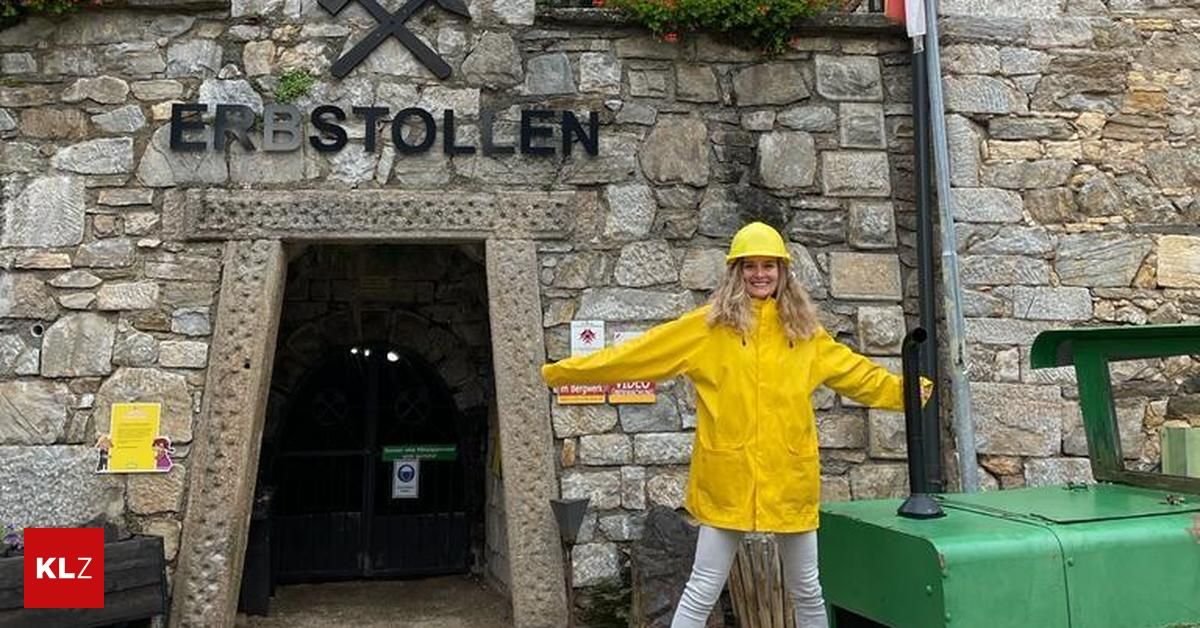 Eine Frau in einem gelben Regenmantel und Helm steht lächelnd vor der Kamera vor dem Eingang eines Tunnels aus Stein.