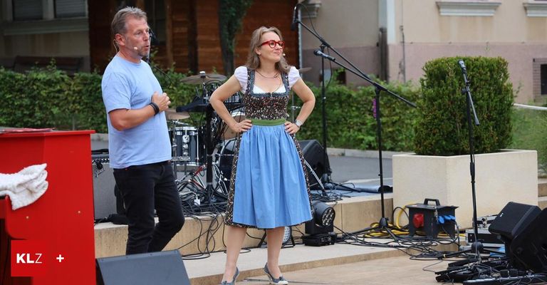Ein Mann und eine Frau stehen mit einem Schlagzeug und Mikrofonen auf der Bühne. Die Frau trägt ein traditionelles Kleid.