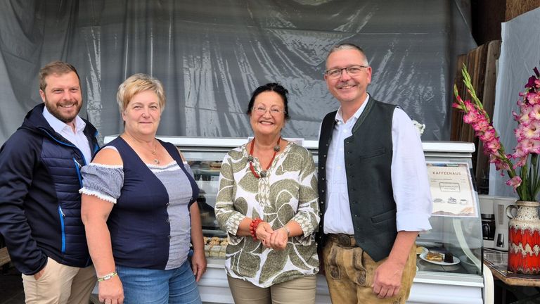 Drei Personen stehen nebeneinander vor einer Bäckerei-Vitrine. Sie lächeln alle und scheinen für ein Foto zu posieren.