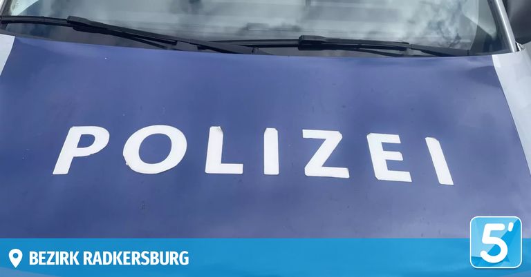 Eine Nahaufnahme der Motorhaube eines Polizeifahrzeugs mit dem Wort 'POLIZEI' in Weiß, der untere Teil hat einen blauen und weißen Rand mit 'ADKERSBURG' darauf.