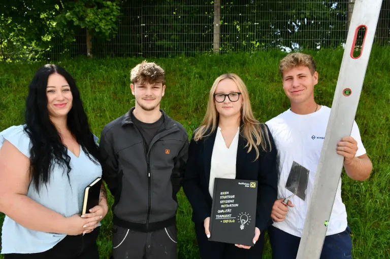 Vier Personen stehen draußen auf einem Feld. Eine Frau hält ein Buch und ein Mann eine Schaufel. Ein anderer Mann hält ein Buch mit 'Ideen, Strategie, Effizienz, Motivation, Qualität, Teamgeist = Erfolg'.