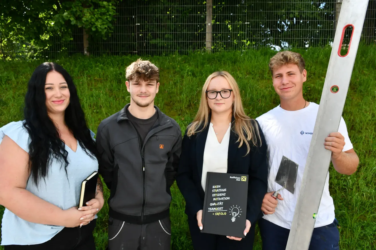 Vier Personen stehen draußen auf einem Feld. Eine Frau hält ein Buch und ein Mann eine Schaufel. Ein anderer Mann hält ein Buch mit 'Ideen, Strategie, Effizienz, Motivation, Qualität, Teamgeist = Erfolg'.