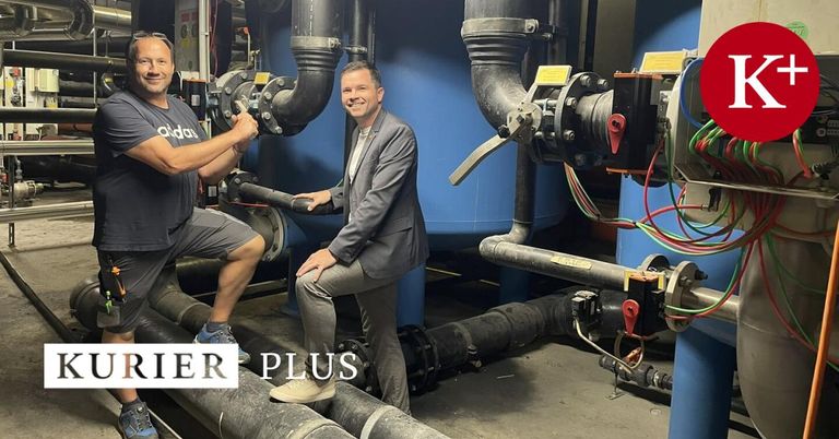 Zwei Männer posieren für ein Foto in einer Fabrik. Ein Mann trägt einen Anzug und der andere trägt ein graues Hemd.