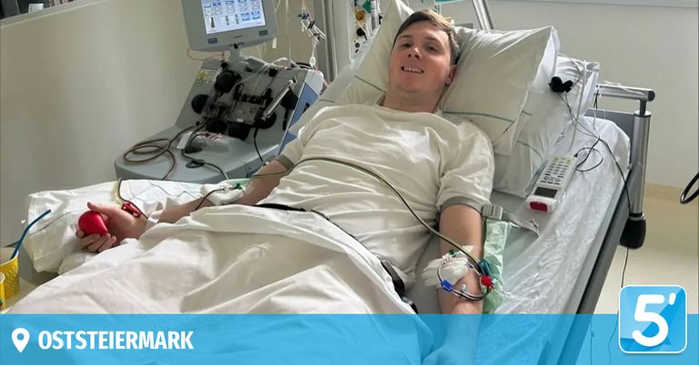Ein Mann liegt mit angeschlossenen medizinischen Geräten in einem Krankenhausbett und lächelt in die Kamera.