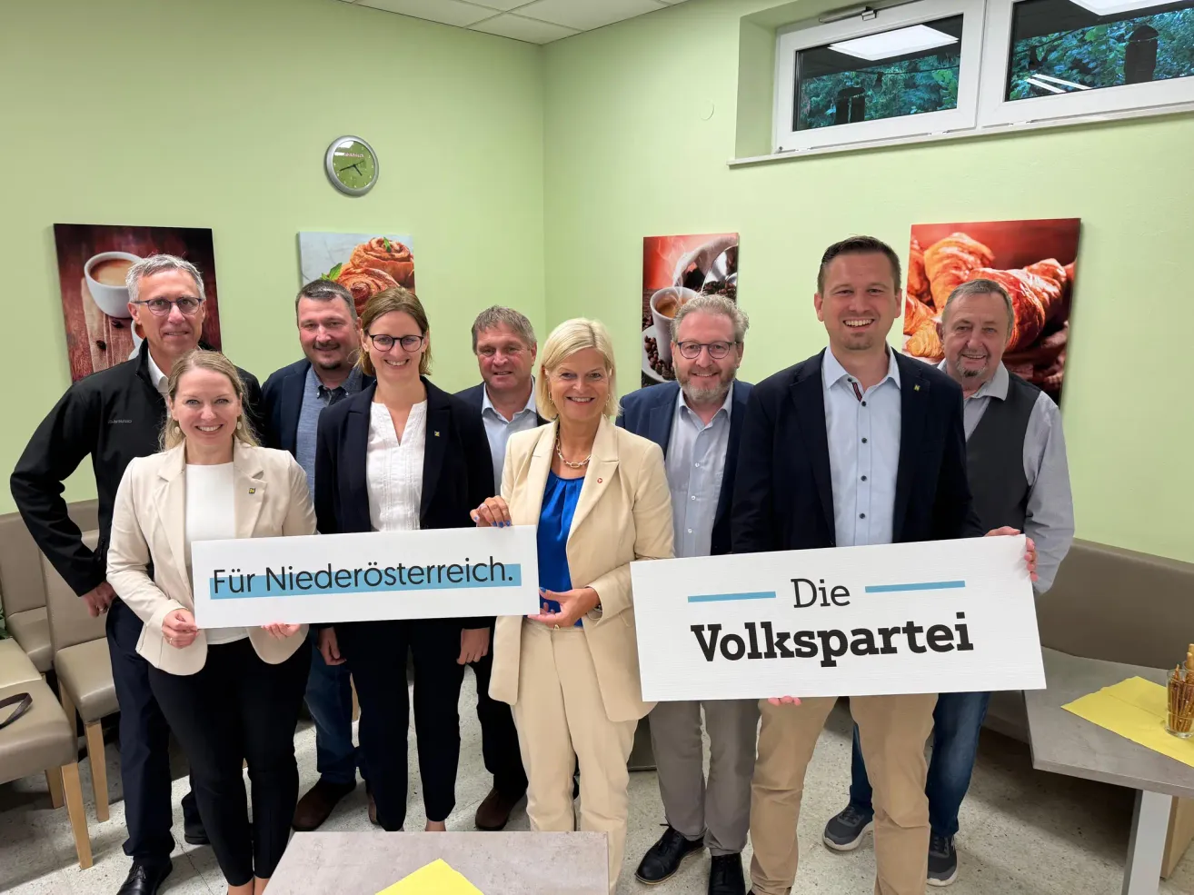 Eine Gruppe von Menschen steht in einem Raum und hält Schilder, die 'Für Niederosterreich' und 'Die Volkspartei' sagen. Sie lächeln und scheinen für ein Foto zu posieren.