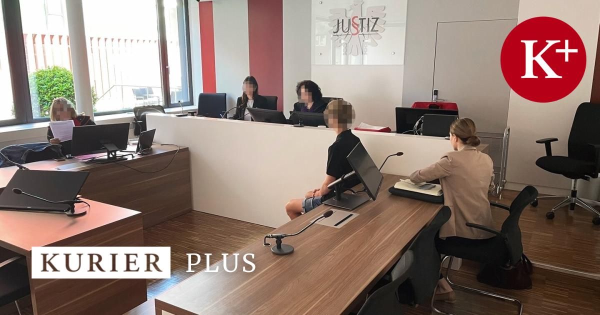 Ein Büro mit mehreren Schreibtischen, Monitoren und sitzenden Personen. Ein Schreibtisch mit der Aufschrift 'ER PLUS' ist sichtbar. Es gibt eine Wand mit Logo und einem Glasfenster.