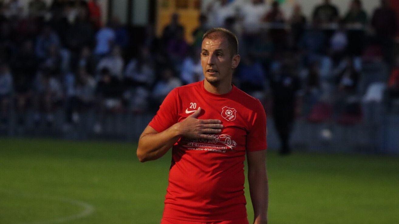 Ein männlicher Fußballspieler mit der Nummer 20 auf seinem roten Trikot steht auf dem Feld und spricht möglicherweise zu den Zuschauern.
