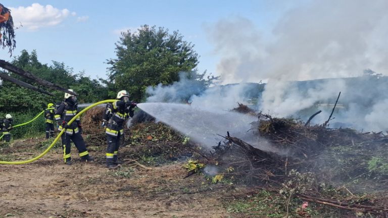 Ein Feuerwehrmann sprüht Wasser aus einem Schlauch auf einen brennenden Haufen von Trümmern im Freien.