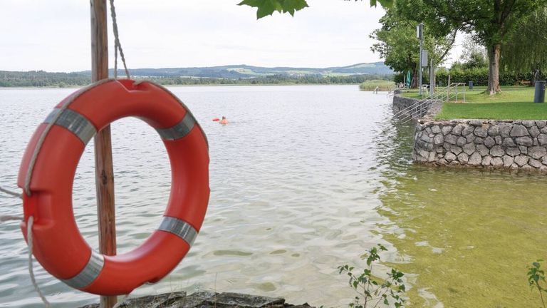 Ein See mit einem Schwimmenden, einem Rettungsring hängend und Bergen in der Ferne.