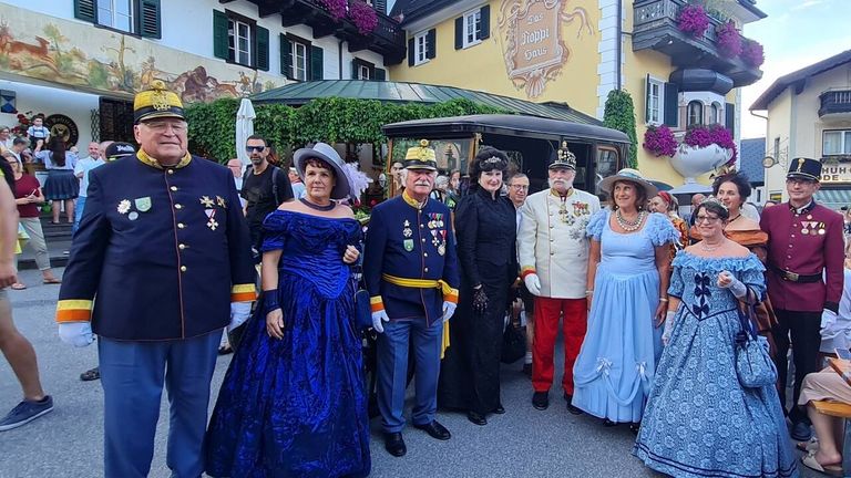 Eine Gruppe von Menschen in historischer Kleidung, darunter Militäruniformen und Kleider, steht vor einer Kutsche vor einem gelben Gebäude mit dem Schild Das Hopfenhaus.