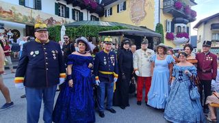 Eine Gruppe von Menschen in historischer Kleidung, darunter Militäruniformen und Kleider, steht vor einer Kutsche vor einem gelben Gebäude mit dem Schild Das Hopfenhaus.