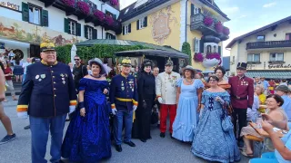 Eine Gruppe von Menschen in historischer Kleidung steht vor einem Gebäude mit lila Blumen und einem Schild mit der Aufschrift 'Das Hopfenhaus'.