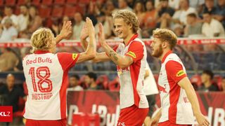 Drei Fußballspieler in roten und weißen Trikots feiern ein Tor. Der Spieler in der Mitte trägt ein Trikot mit der Nummer 8 und einem Bullenlogo.