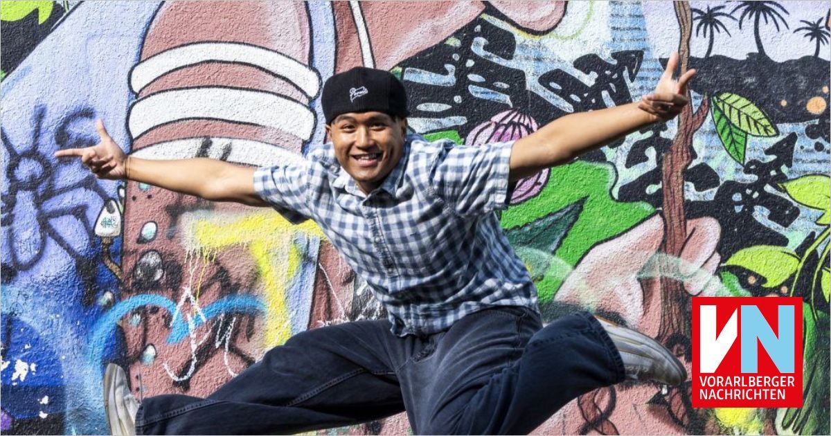 Ein Mann in einem karierten Hemd und Jeans springt vor einer mit Graffiti bedeckten Wand.