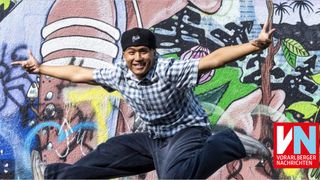 Ein Mann in einem karierten Hemd und Jeans springt vor einer mit Graffiti bedeckten Wand.