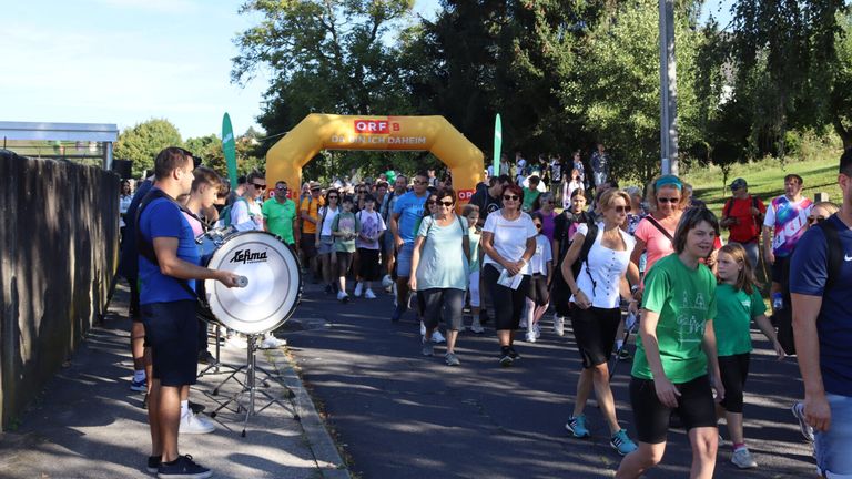 Teilnehmer gehen durch einen gelben Bogen mit der Aufschrift 'ORF B Da Bin Ich Daheim' bei einem Marathon-Event, mit einem Schlagzeuger im Hintergrund.
