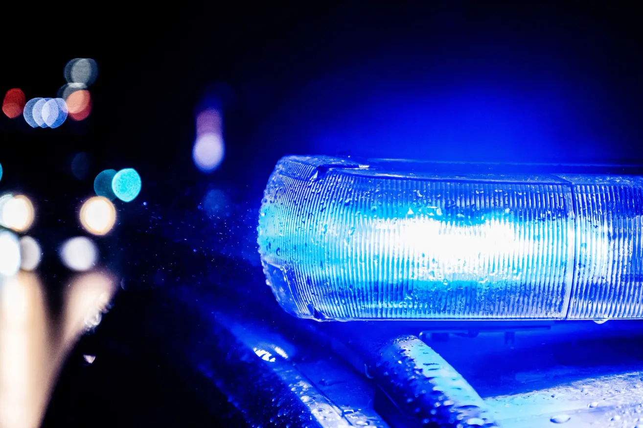 Eine Nahaufnahme des blauen Sirenenlichts eines Polizeiwagens. Das Licht ist nass und leuchtet hell vor einem dunklen Hintergrund.