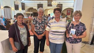 Vier Frauen stehen in einer Kirche. Die Frau auf der linken Seite trägt eine Jacke. Die Frau neben ihr trägt ein Blumenhemd und Jeans. Die beiden Frauen auf der rechten Seite tragen gestreifte Hemden.