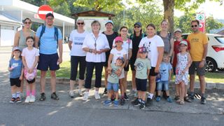 Eine Gruppe von Menschen, einschließlich Erwachsener und Kindern, posiert für ein Foto in einem Park. Sie stehen vor einem Holzschild und Bäumen.