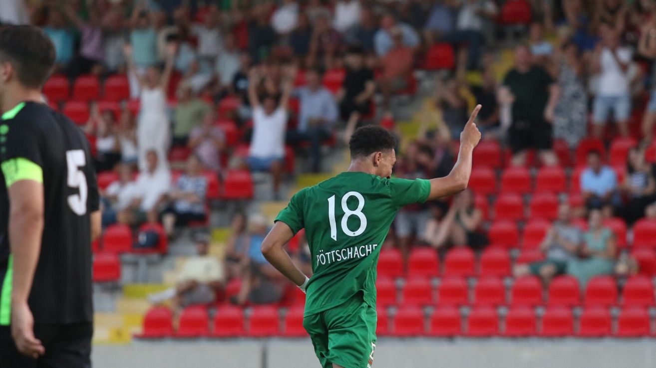 Ein Fußballspieler in einem grünen Trikot mit der Nummer 18 feiert vor Publikum ein Tor.