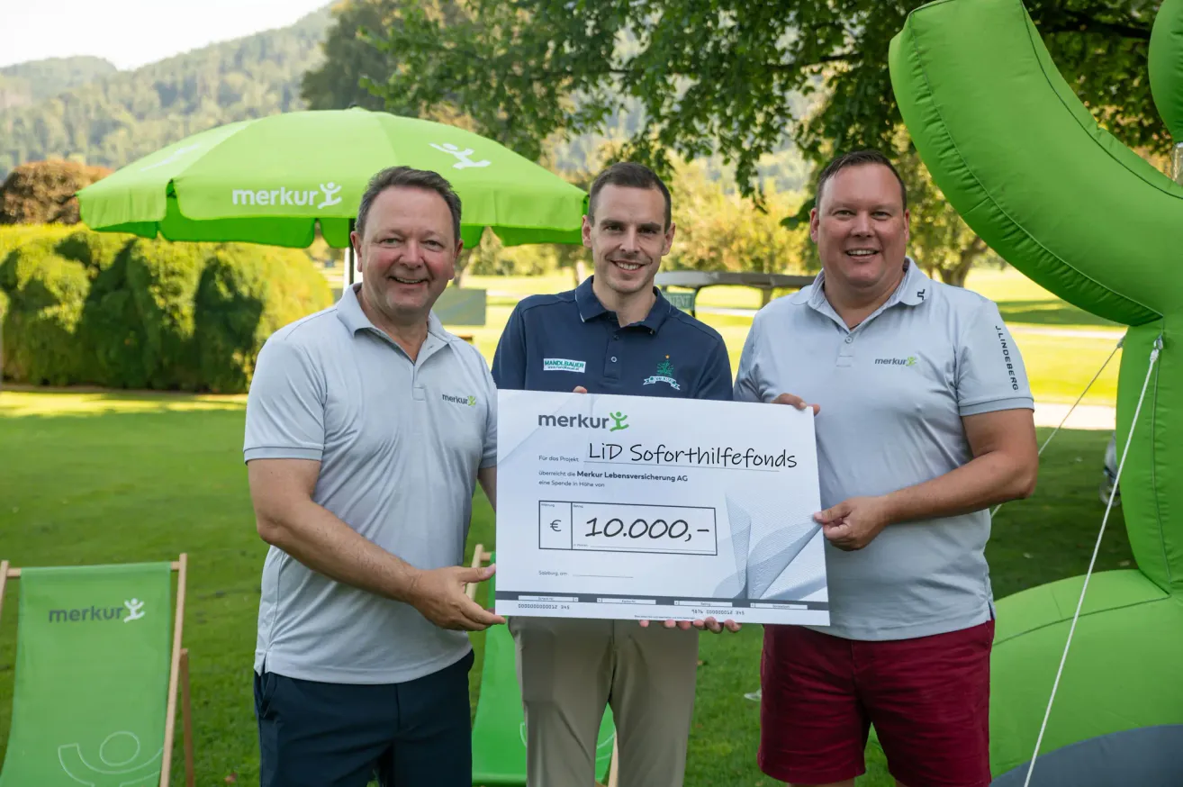 Drei Männer stehen draußen und halten einen großen Scheck über 10.000 Euro, lächeln, mit einem grünen Schirm im Hintergrund.