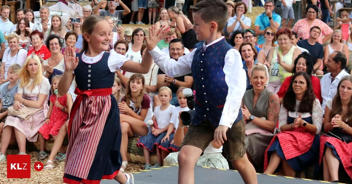 Zwei Kinder führen einen Tanz auf der Bühne vor einem Publikum auf, beide in traditioneller Kleidung. Das Publikum klatscht und lächelt.
