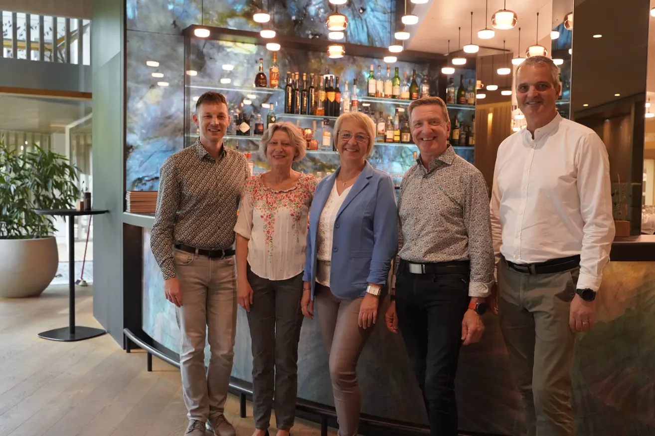 Fünf Personen, zwei Männer und drei Frauen, stehen lächelnd vor einer Bartheke für ein Foto.