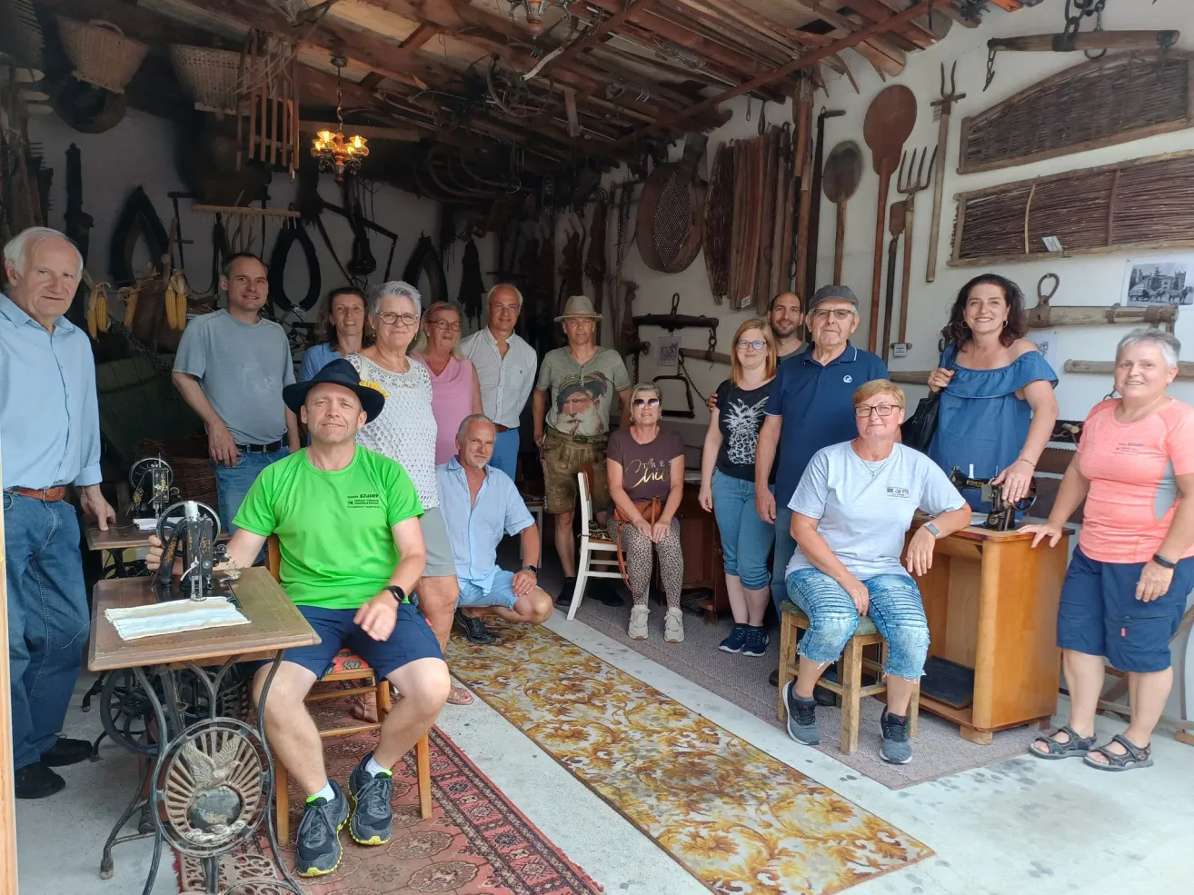 Eine Gruppe von Menschen posiert für ein Foto in einer Werkstatt. Sie stehen und sitzen in einem Raum mit alten Werkzeugen, die an der Wand hängen.