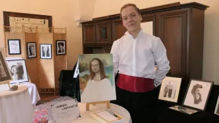 Ein junger Mann steht neben einem Mona-Lisa-Gemälde auf einem Tisch, umgeben von gerahmten Bildern und Kunstwerken. Er trägt ein weißes Hemd und einen roten Gürtel.