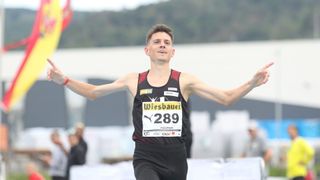 Ein Mann in einem schwarzen und roten Trikot mit 'Wiesbauer' und der Nummer 289 feiert nach einem Rennen mit ausgestreckten Armen.