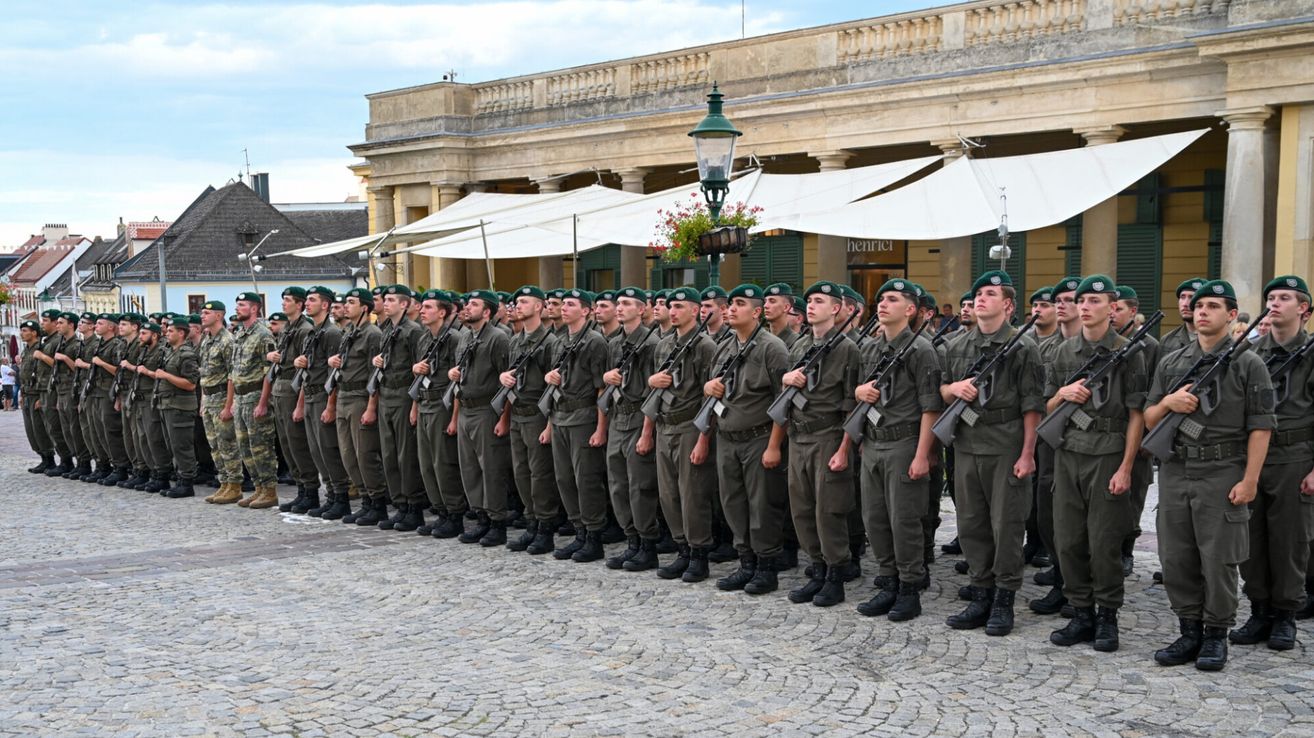 Eine Gruppe von Soldaten in Uniform steht in einer Reihe vor einem großen Gebäude mit Säulen und Markisen.