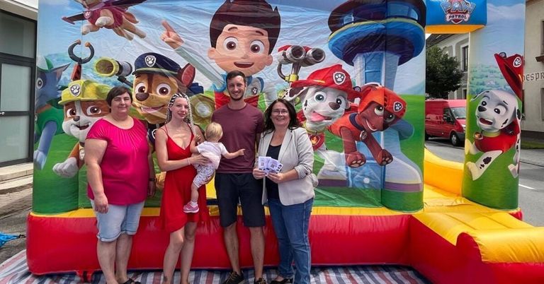 Vier Personen stehen vor einem Paw Patrol-inspirierten Aufblasbar, wobei eine Frau ein Baby und ein Mann Eintrittskarten hält.