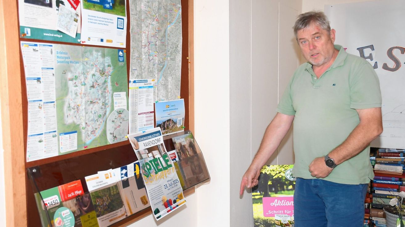 Ein Mann in einem grünen Shirt und blauer Hose steht neben einer Pinnwand mit Karten und Veranstaltungsflyern. Ein Flyer hat ein farbenfrohes Bild und den Text 'Spiele'.