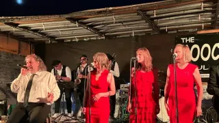 Eine Band tritt bei Nacht auf der Bühne auf, mit zwei Frauen in roten Kleidern, die singen, und anderen, die Instrumente spielen.