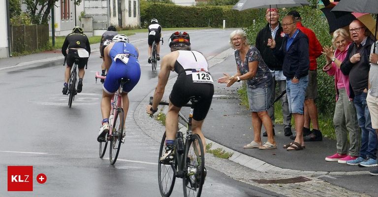 Eine Gruppe von Radfahrern in einem Rennen mit Zuschauern, die jubeln. Eine ältere Frau spricht mit einem Radfahrer mit der Nummer 125.