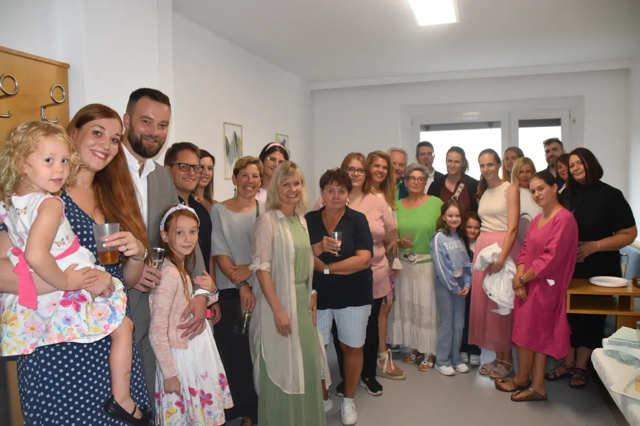 Eine Gruppe von Menschen, einschließlich Erwachsener und Kindern, posiert für ein Foto in einem Raum. Sie alle lächeln und scheinen Spaß zu haben. Einige halten Gläser mit Getränken.
