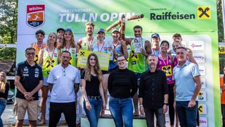 Sieger des Tulln Open Events posieren mit Medaillen und Trophäen. Zwei Frauen stehen vorne, lächeln, während andere dahinter Trophäen halten. Ein Banner steht 'Tulln Open'.