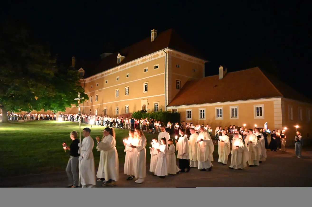 Eine Gruppe von Menschen in weißen Gewändern hält Kerzen vor einem großen Gebäude bei Nacht.