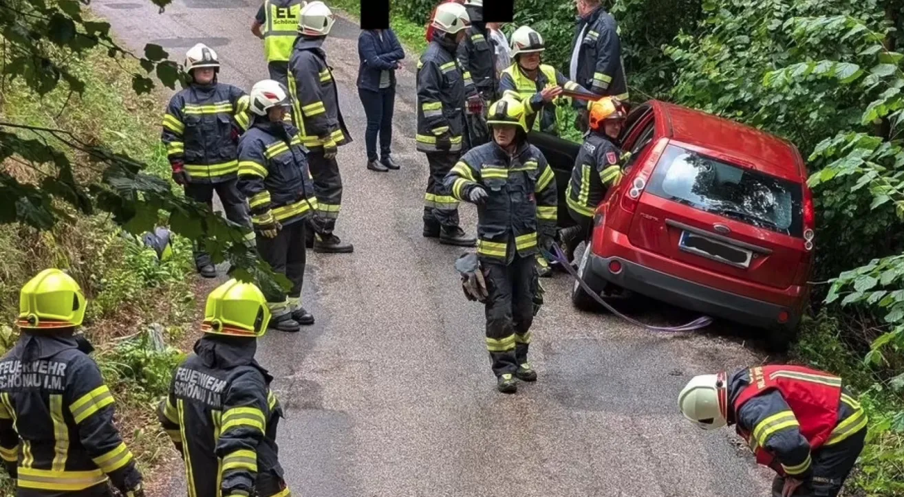 Eine Gruppe von Feuerwehrleuten in Uniform steht am Straßenrand, einer zieht eine Autotür.