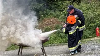 Ein Feuerwehrmann zeigt einem Kind, wie man einen Feuerlöscher benutzt und richtet den Strahl auf ein brennendes Objekt auf einem kleinen Grill.