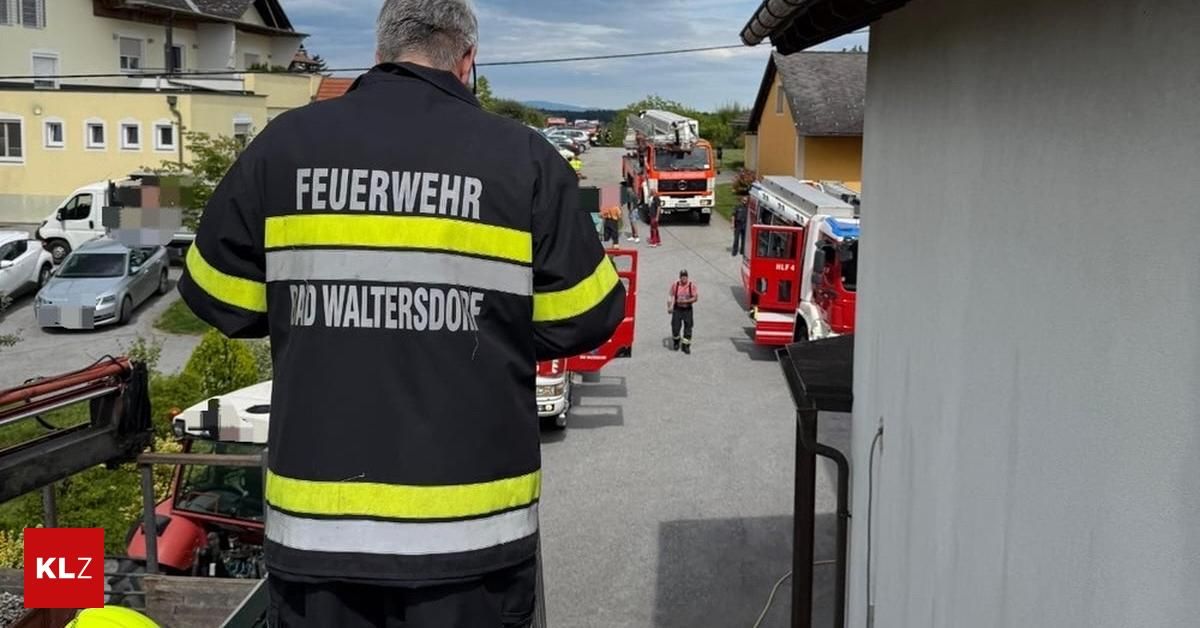 Ein Feuerwehrmann von Rad Waltersdorf steht auf einem Parkplatz mit Feuerwehrwagen. Menschen sind versammelt, möglicherweise im Einsatz bei einem Notfall.